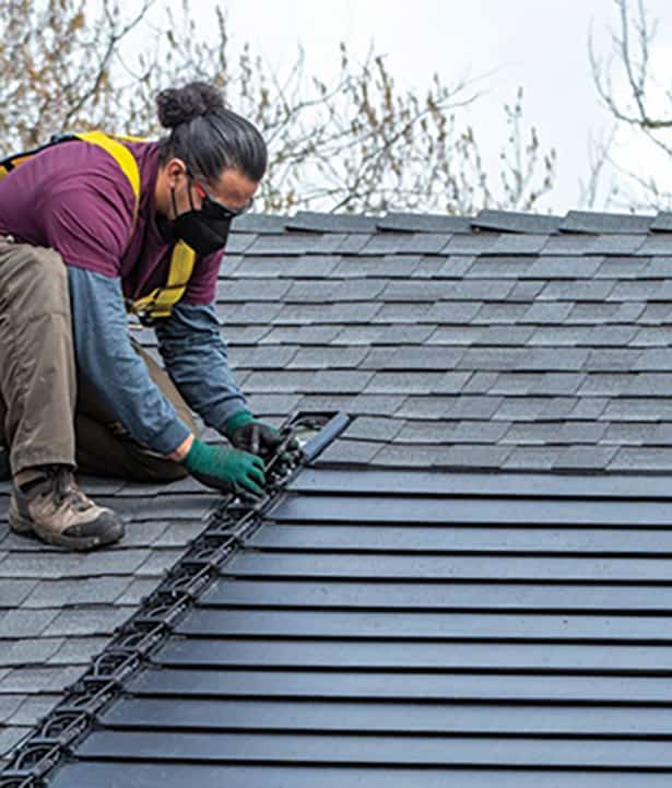 A man installing solar shingles on a roof with gloves.