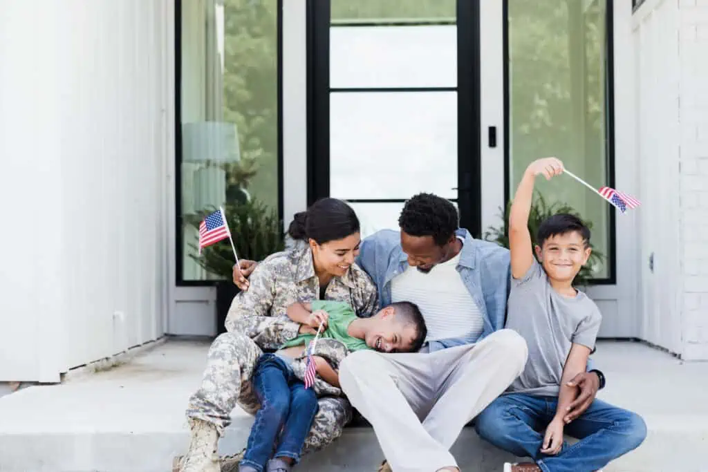 A family celebrates Veterans Day together while holding American flags on the steps of their home.