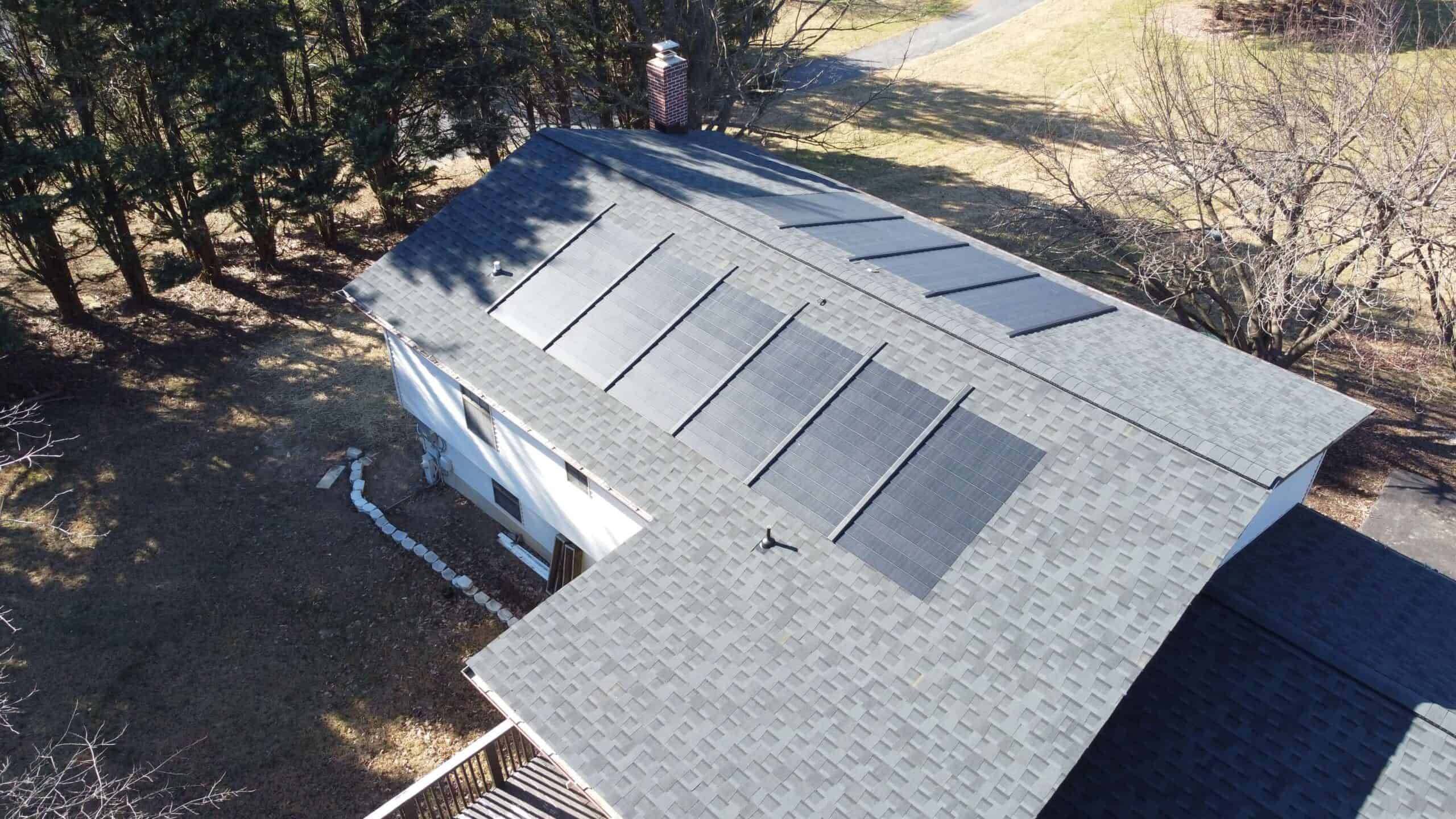 An aerial view of a house with solar shingles on the roof. Learn how to buy solar shingles.