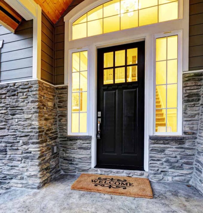 A black door with a welcome mat in front of the entrance of a home.